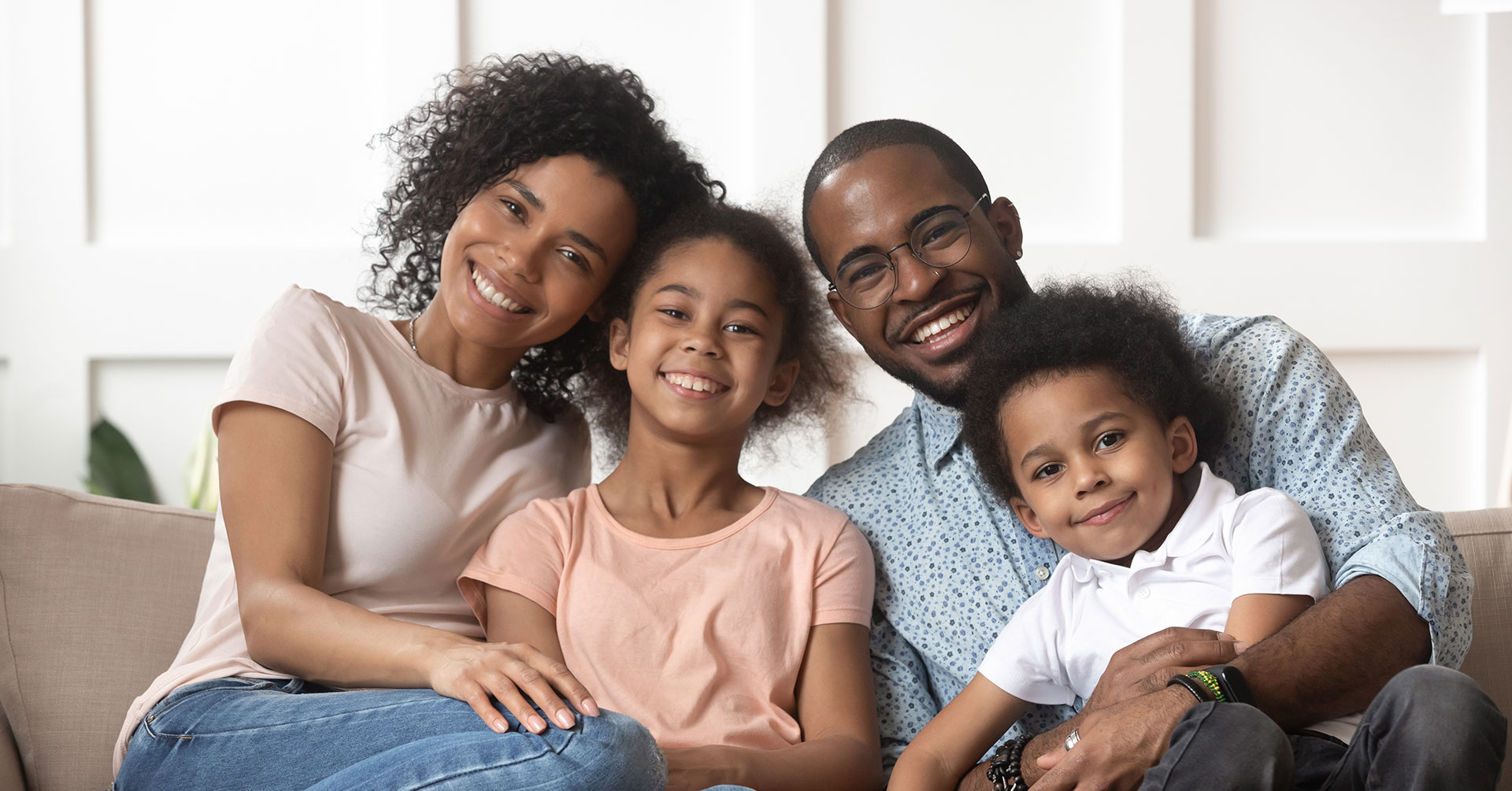 Family of four, including two adults and two children, gathered on a couch for a portrait.