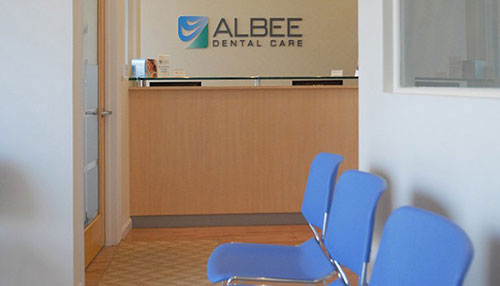 A dental office reception area with a logo and signage, featuring a blue chair and a modern design.
