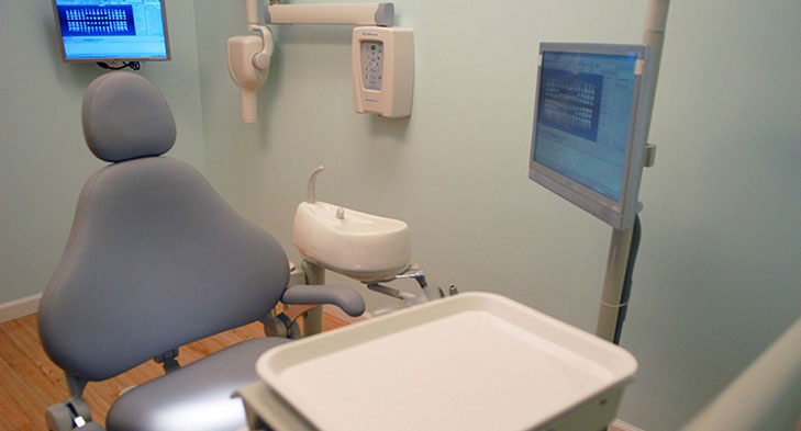 An image of a dental office interior, featuring a dental chair and a dental examination room.
